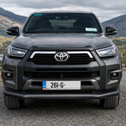 A dark gray Toyota Hilar pickup truck is parked on a gravel path and installed front black bar